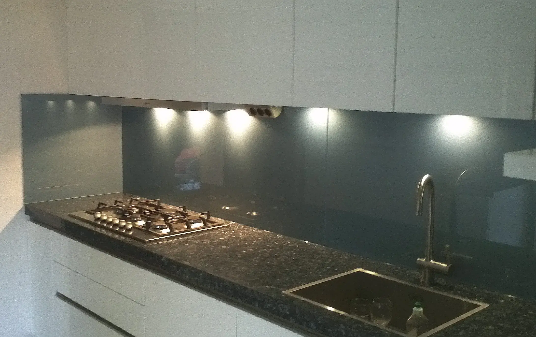 Küchen-Umbau mit Gaskochfeld, neuer Arbeitsplatte aus schwarzem Granit (Labrador Grey 6 cm Dicke) und Glasrückwände in Grau.