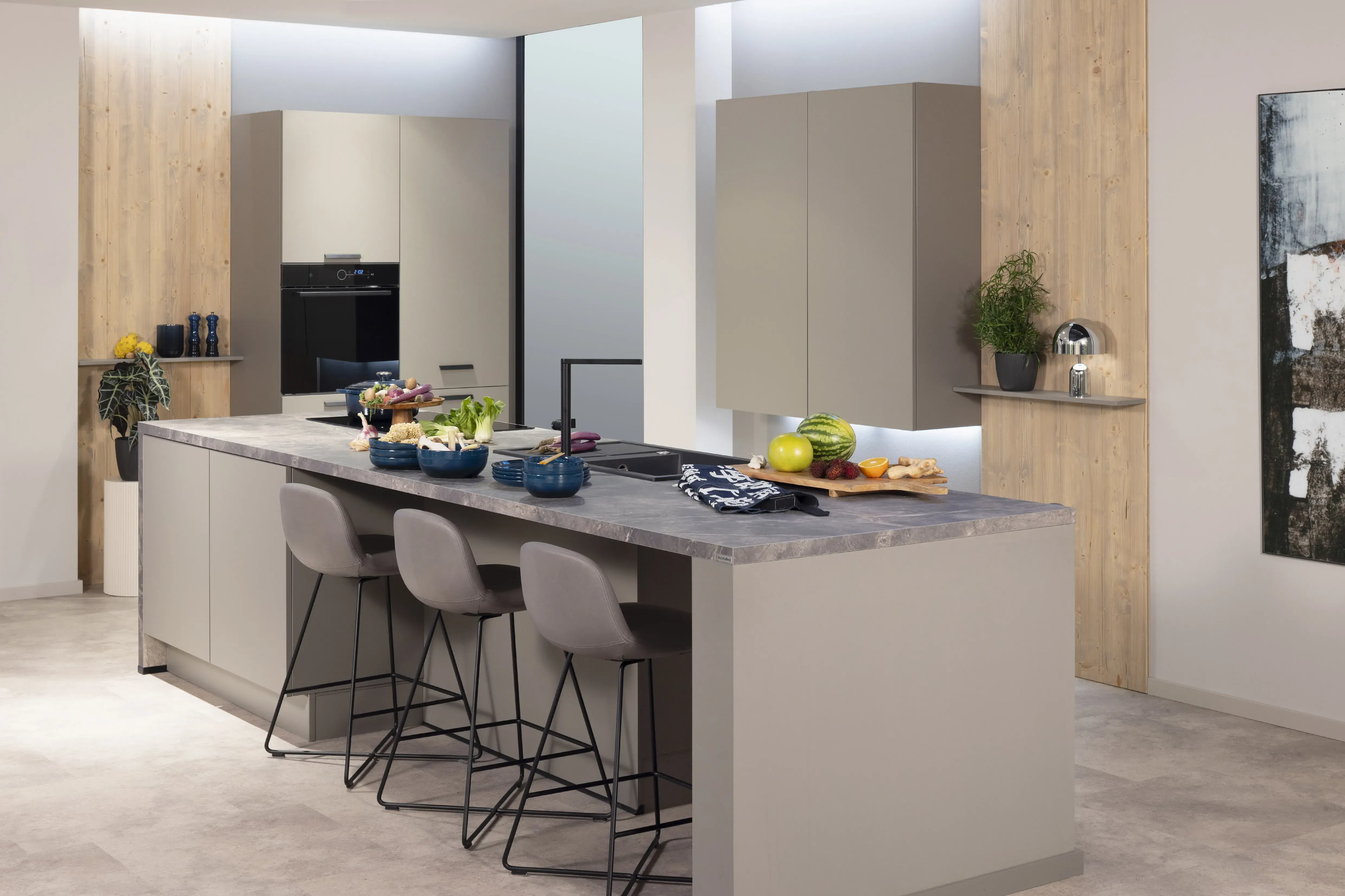 Moderne Küche mit Kücheninsel, Obstschalen und drei grauen Barhockern.
